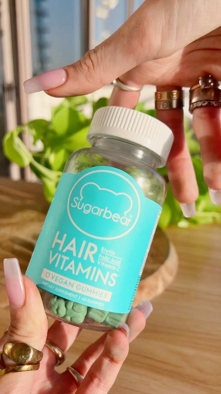 Hands holding a bottle of SugarBearHair hair vitamins with green gummy supplements inside.