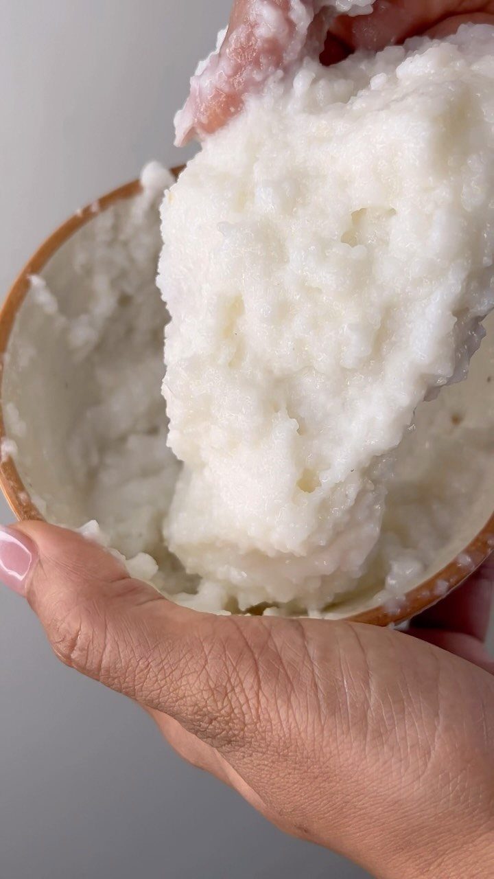 White creamy hair mask being lifted from a brown bowl by hands.