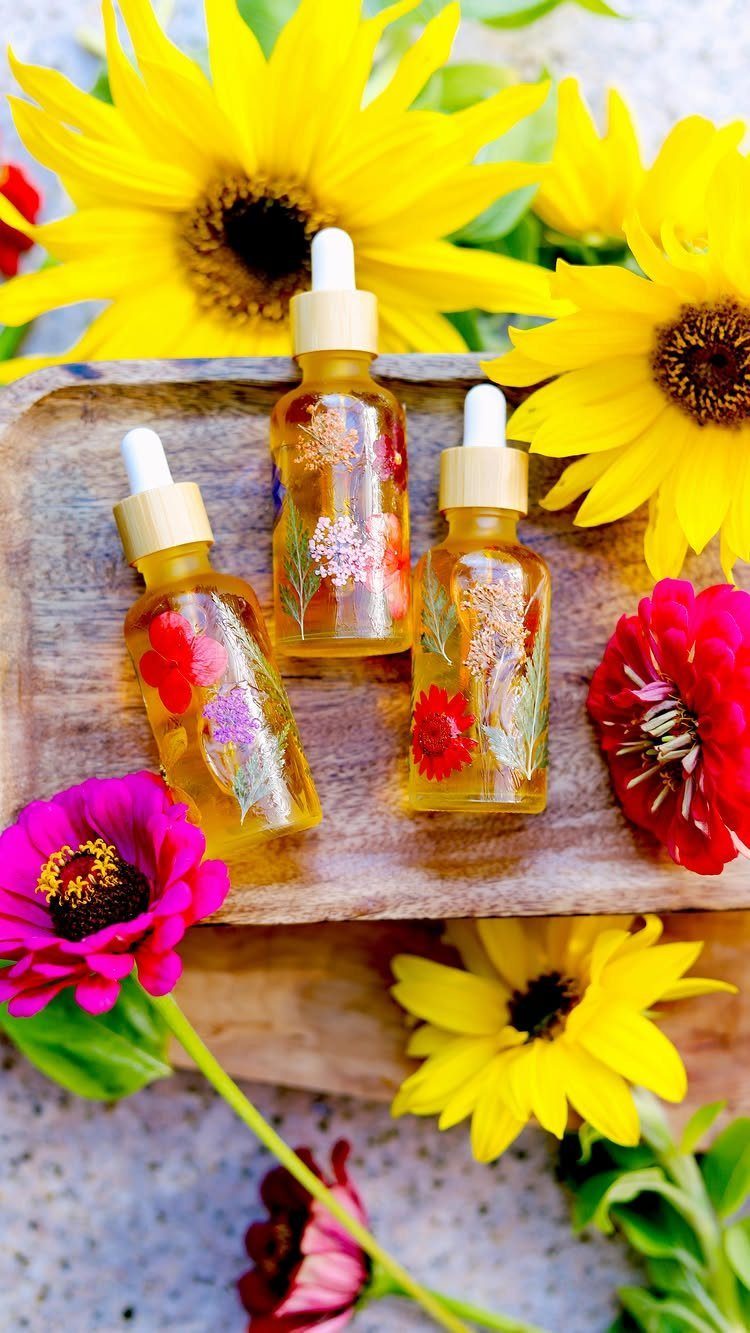 Three glass dropper bottles of botanical oil surrounded by colorful sunflowers and zinnias.