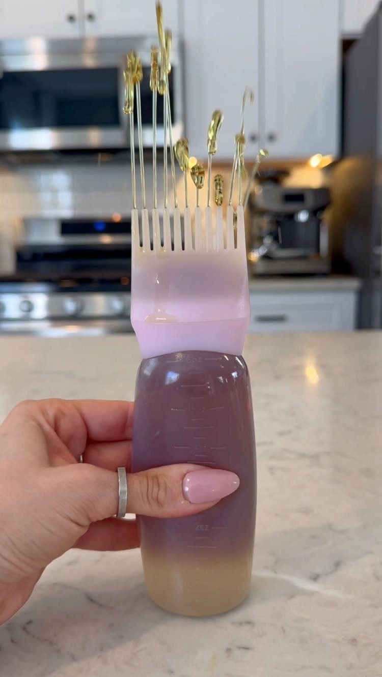 Purple bottle with a pink scalp applicator brush held by a hand in a kitchen