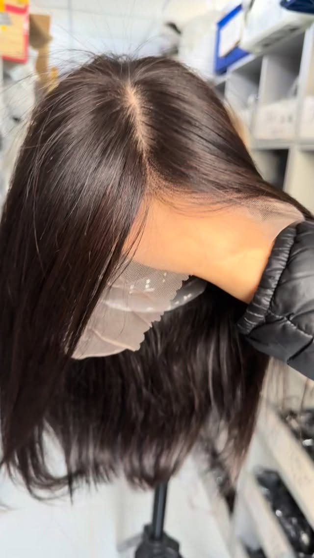 Dark brown hair being lifted to show a lace hairpiece attached to the scalp.