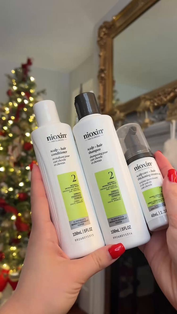 Three Nioxin hair care bottles held by a person against a festive background.