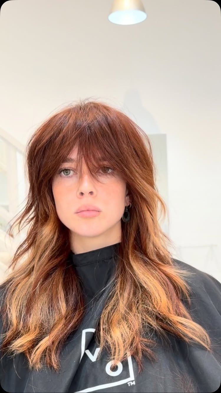 Woman with auburn shag haircut featuring heavy layered bangs and face-framing layers.