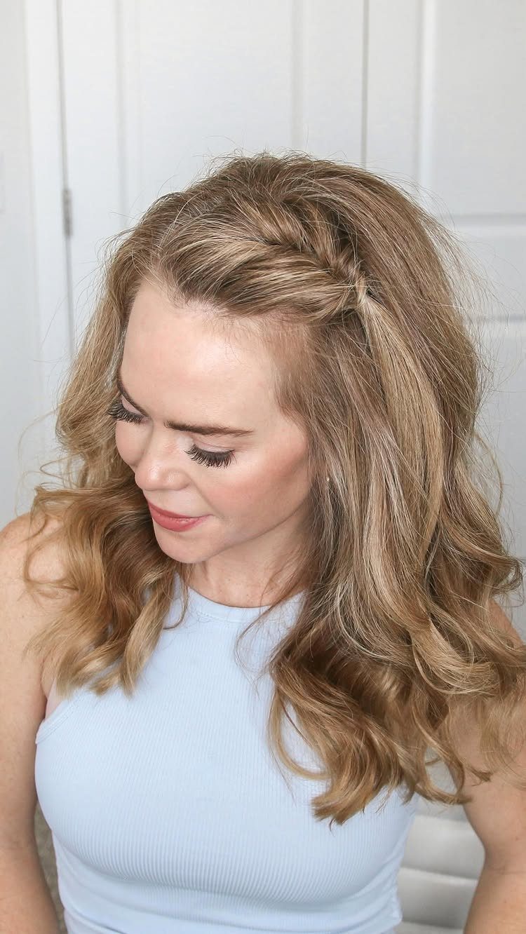 Woman with blonde wavy hair featuring a half-up twist hairstyle secured at the side.