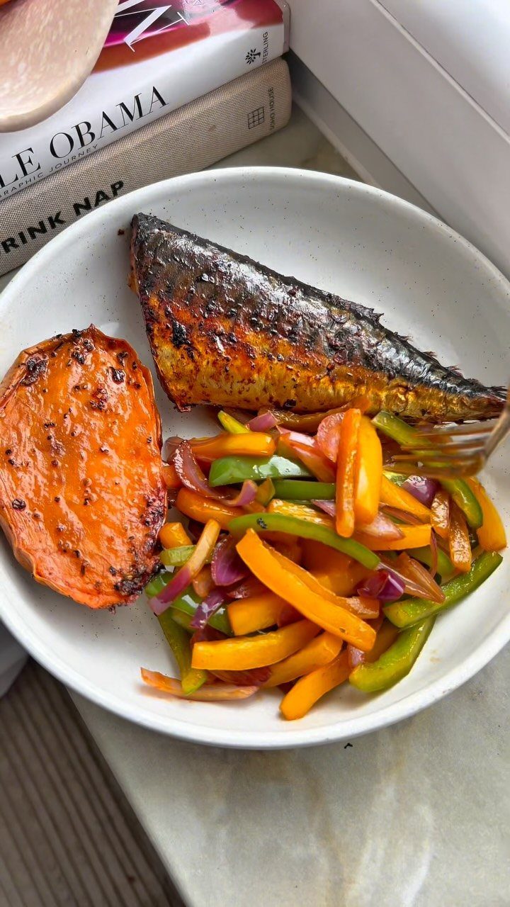 Grilled fish, roasted sweet potato, and sautéed bell peppers in a white bowl.