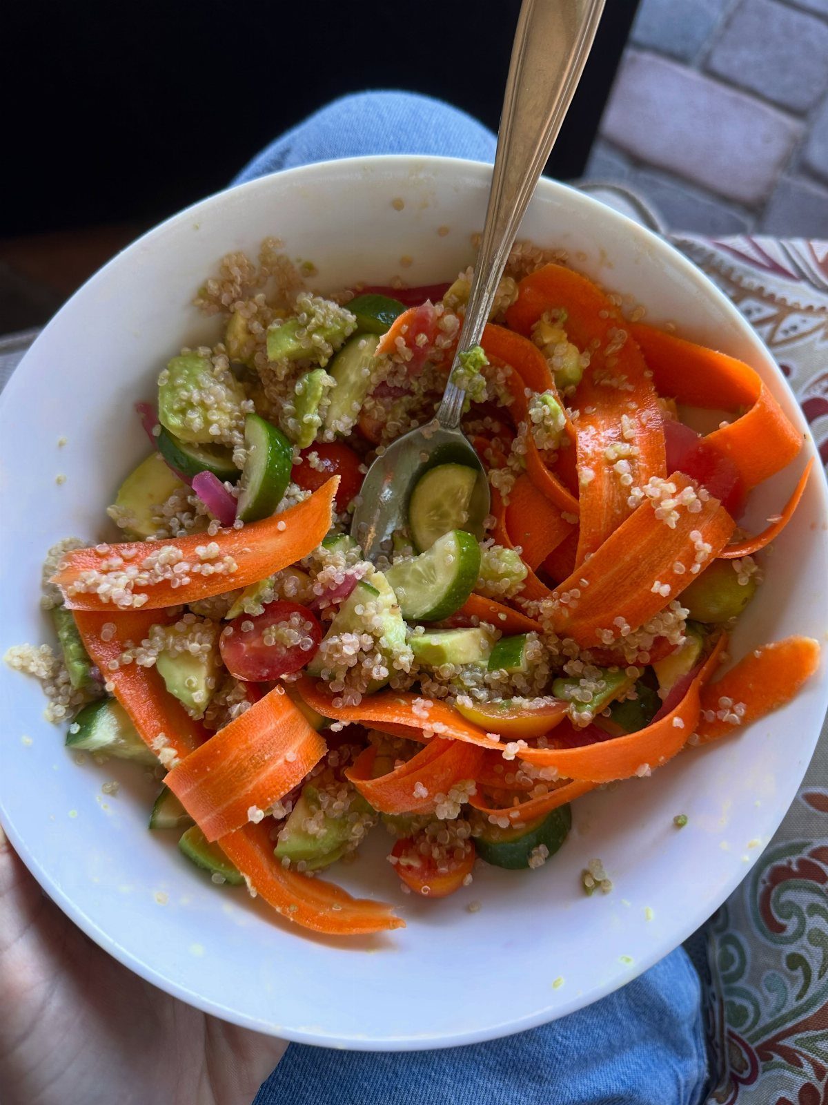 Quinoa salad with orange carrot ribbons, cucumbers, and tomatoes in a white bowl