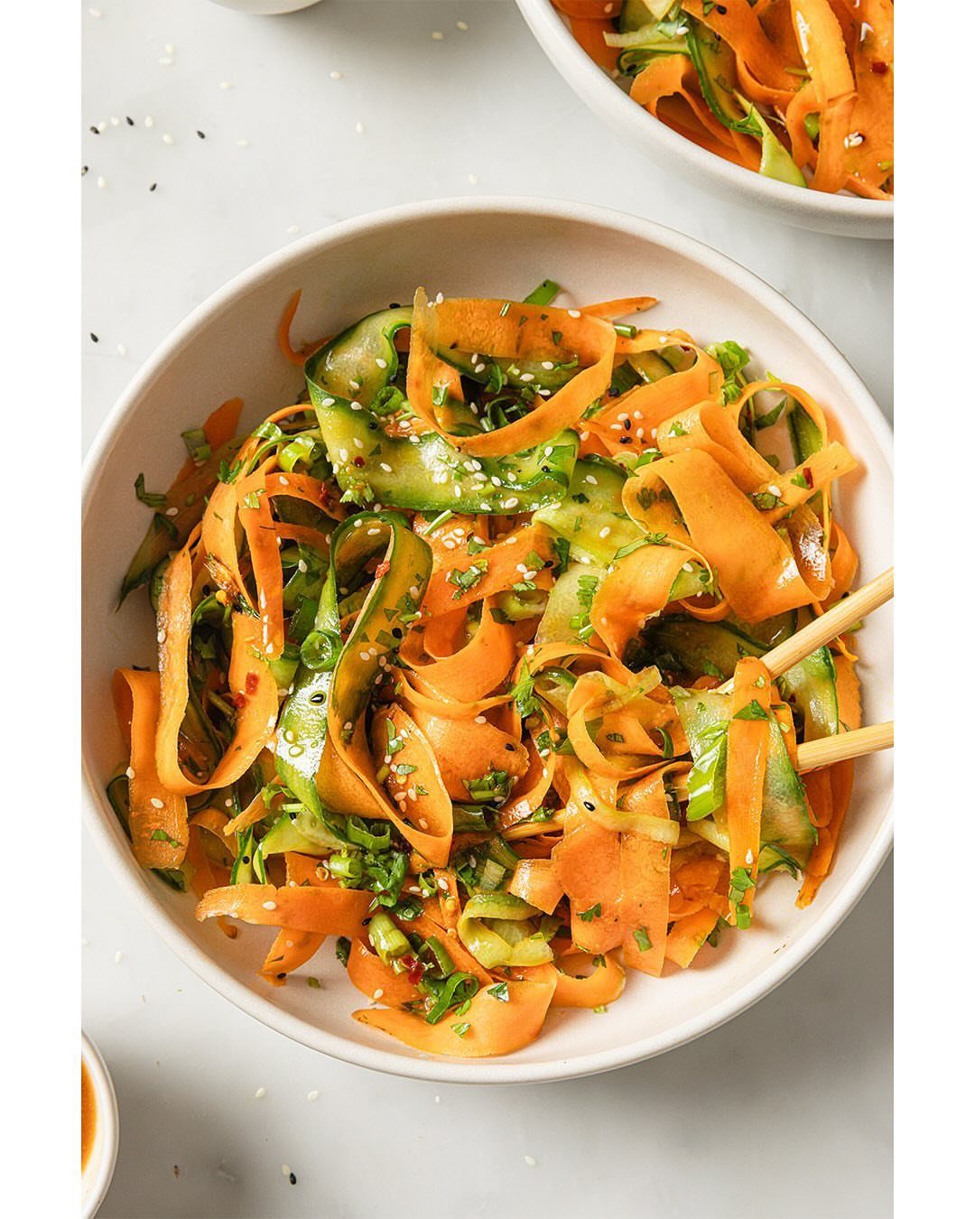 Spiralized carrot and cucumber salad in a white bowl with wooden chopsticks.