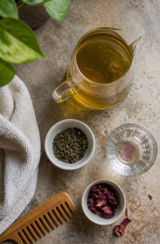 Green tea in a cup beside leaves and a bowl for a hair rinse