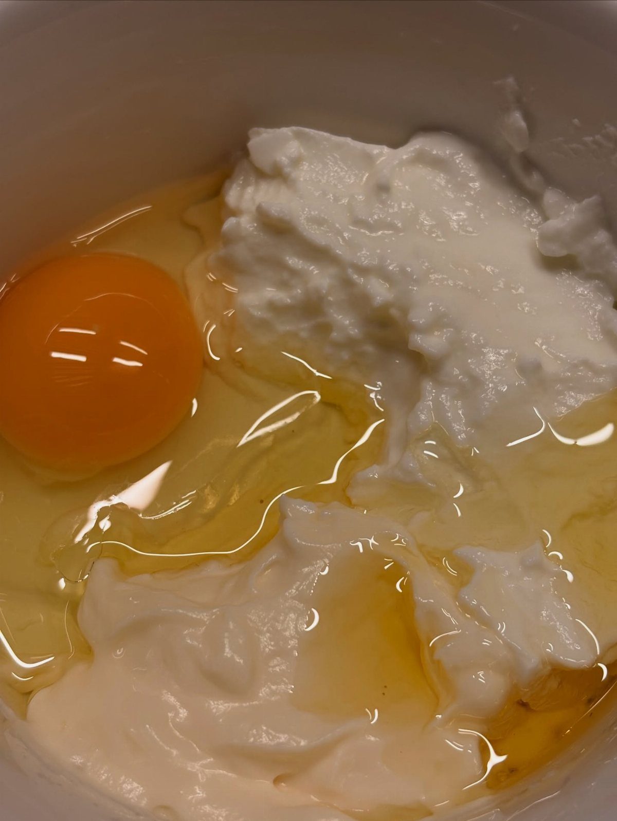 Raw egg and white yogurt mixed together in a white ceramic bowl