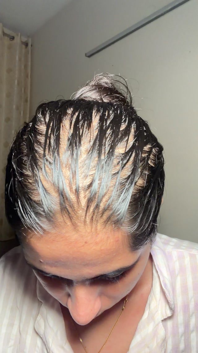 Person with dark hair coated in a white hair mask gathered in a bun