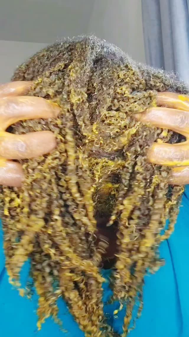 Hands applying a yellowish-green hair mask to curly, textured hair.