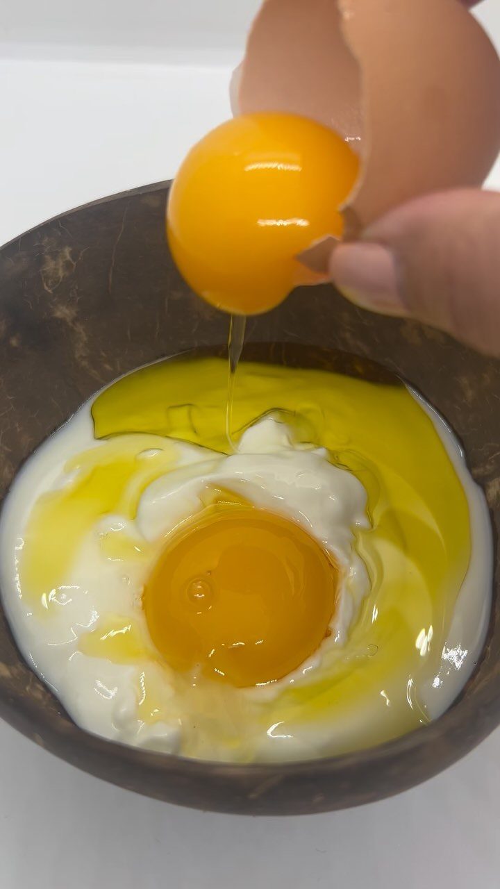 Raw egg being cracked into a bowl with yogurt and oil.