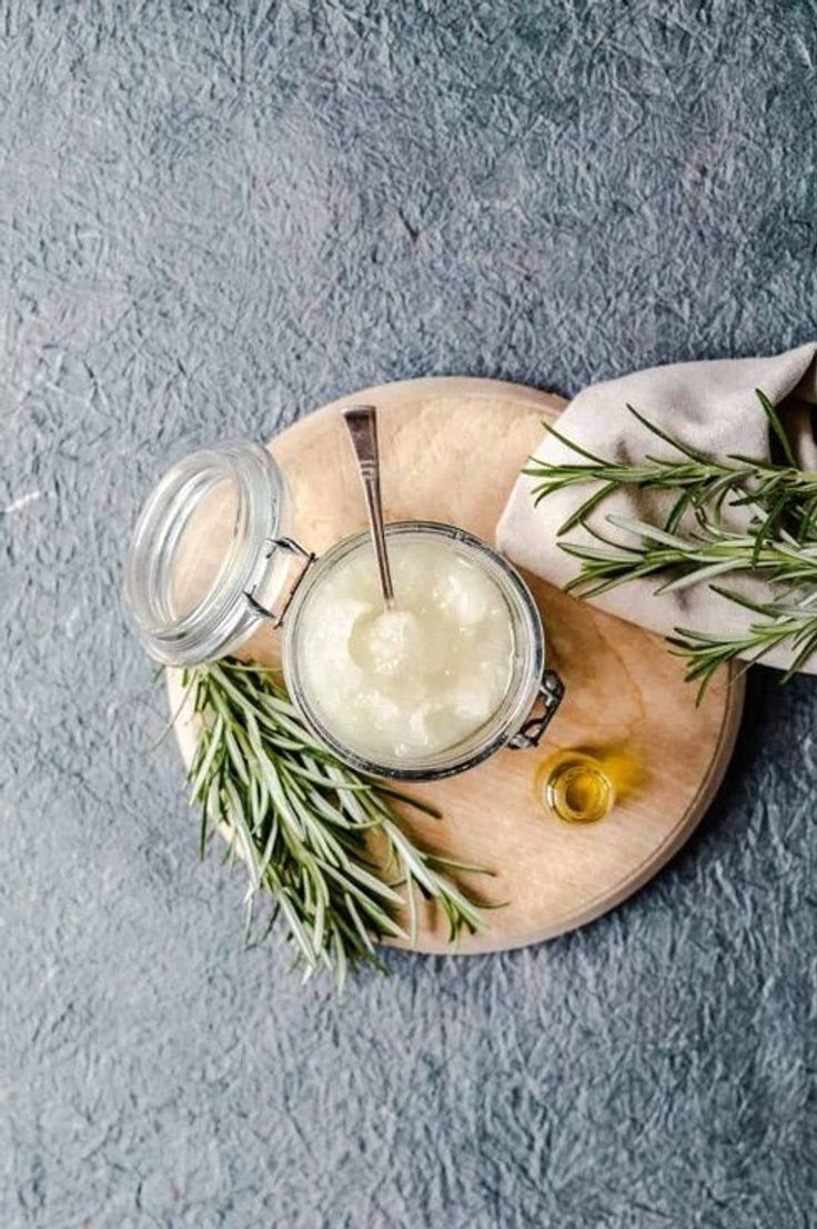 White grainy scrub in a glass jar with rosemary and oil on wood.