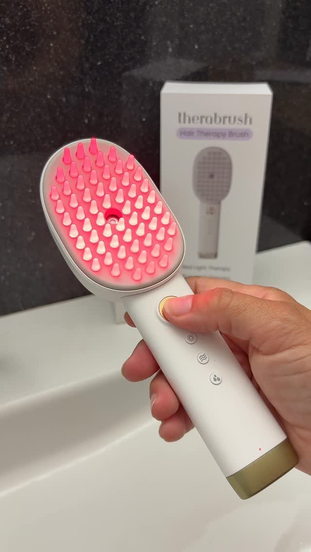 White electronic hair brush with pink bristles and a glowing red light handle.