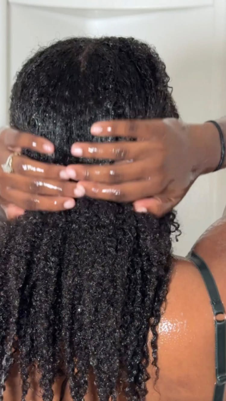 Person massaging their wet, curly black hair and scalp with both hands.