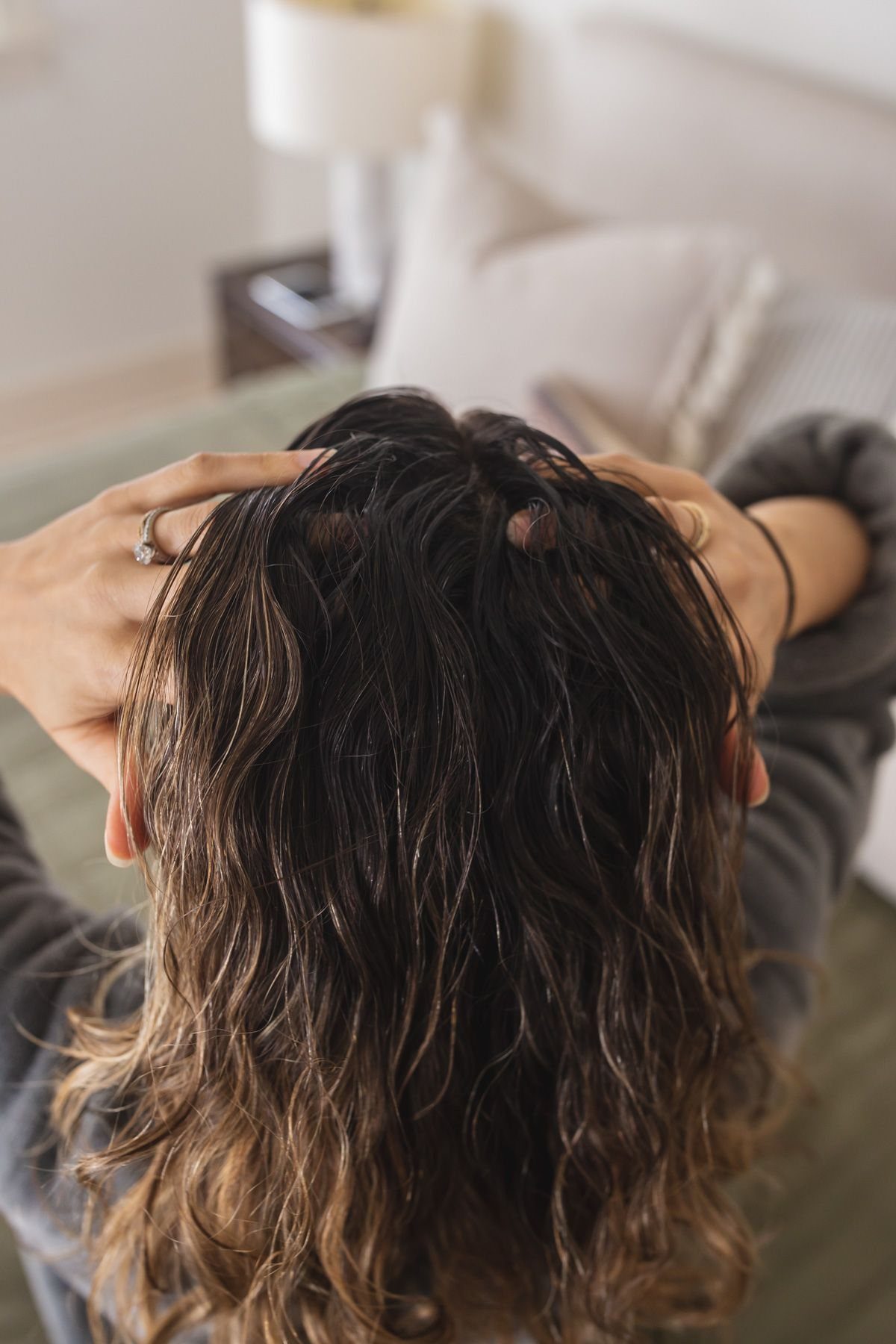 Person massaging oil into the scalp of their wavy brown hair from behind.