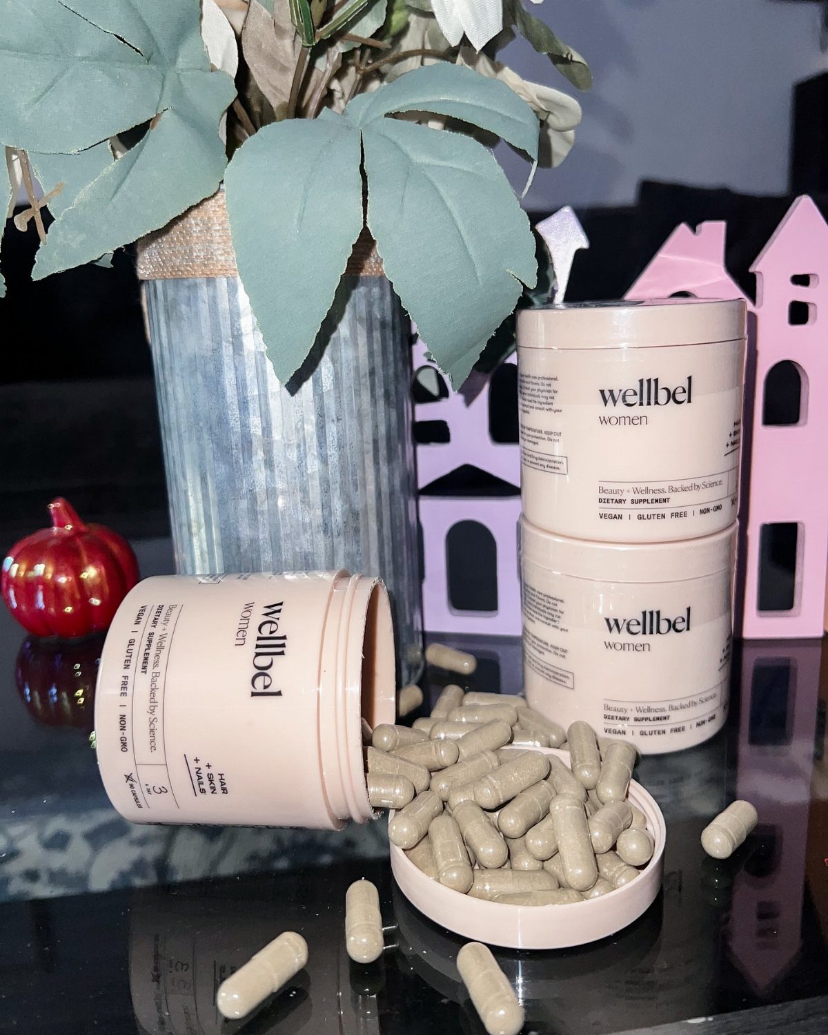 Wellbel Women supplement jars with beige capsules spilled on a reflective black surface.