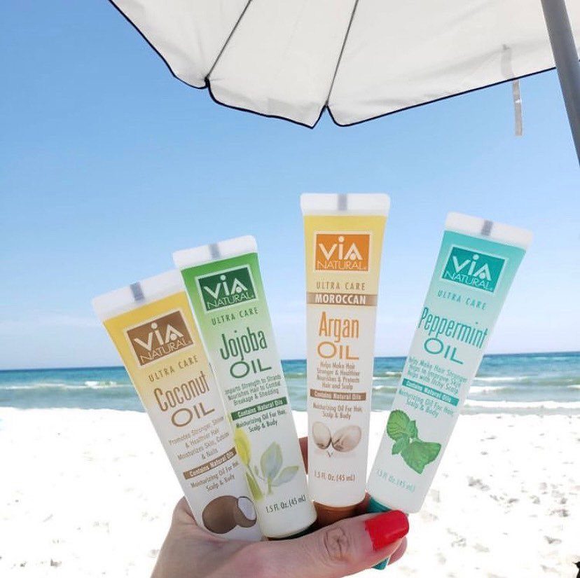 Four tubes of Via Natural hair oils, including peppermint oil, held at a beach.