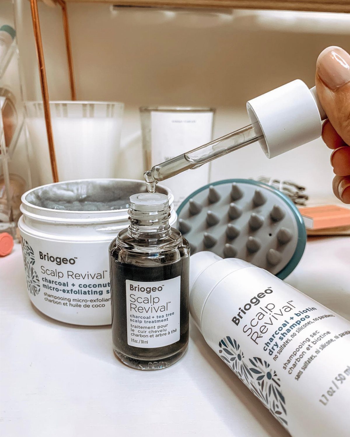 Briogeo charcoal scalp scrub and treatment products with a grey scalp massager tool.