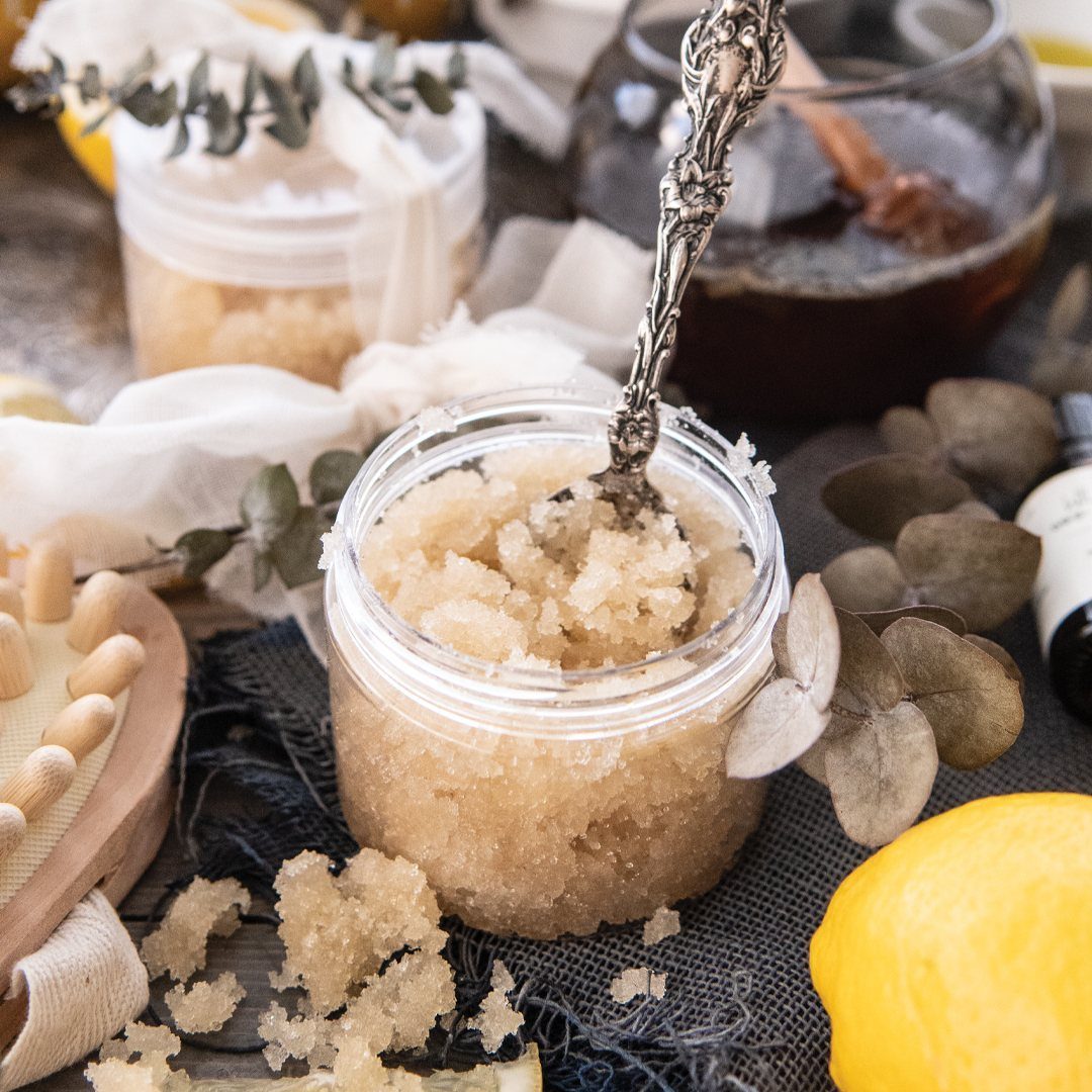 Granular brown scrub in a plastic jar with a silver spoon and lemon.