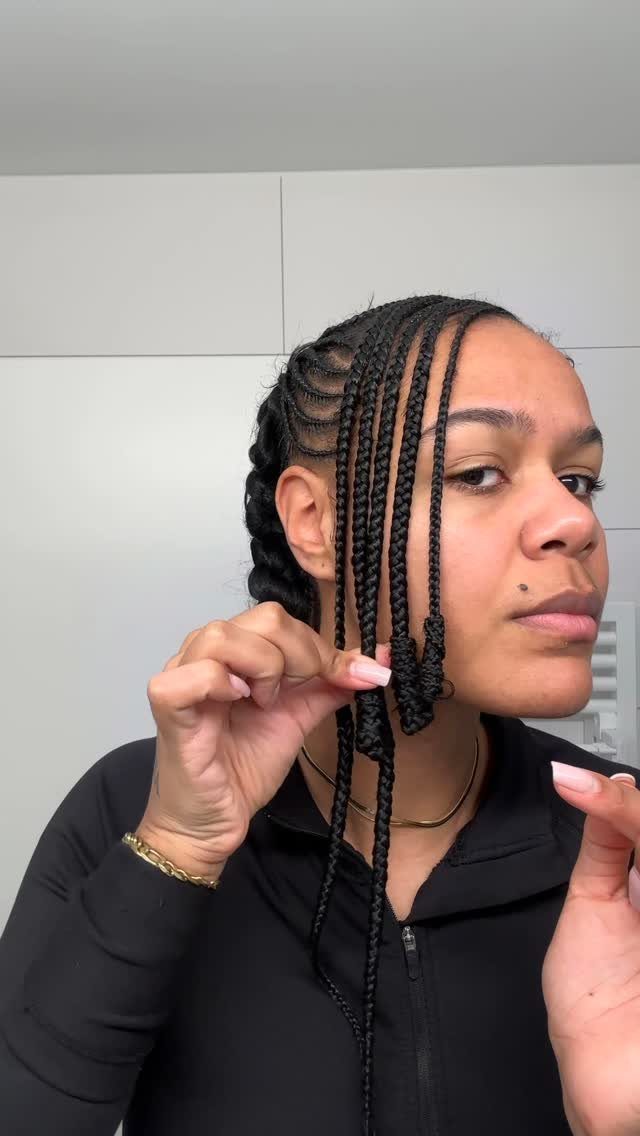 Woman with cornrows and individual braids wearing a black zip-up top.