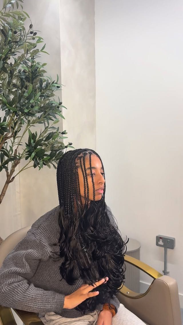 Woman with long dark knotless braids and curly ends wearing a grey sweater.