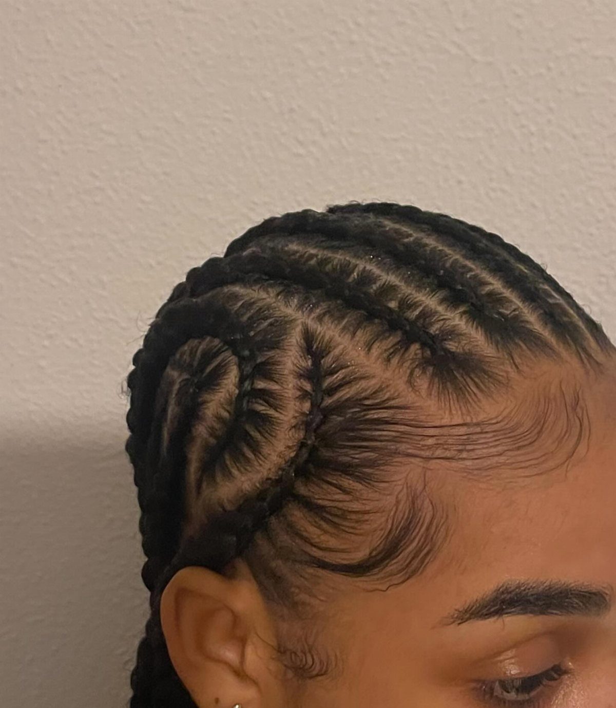 Curved patterned cornrow braids on a person's scalp with styled edges.
