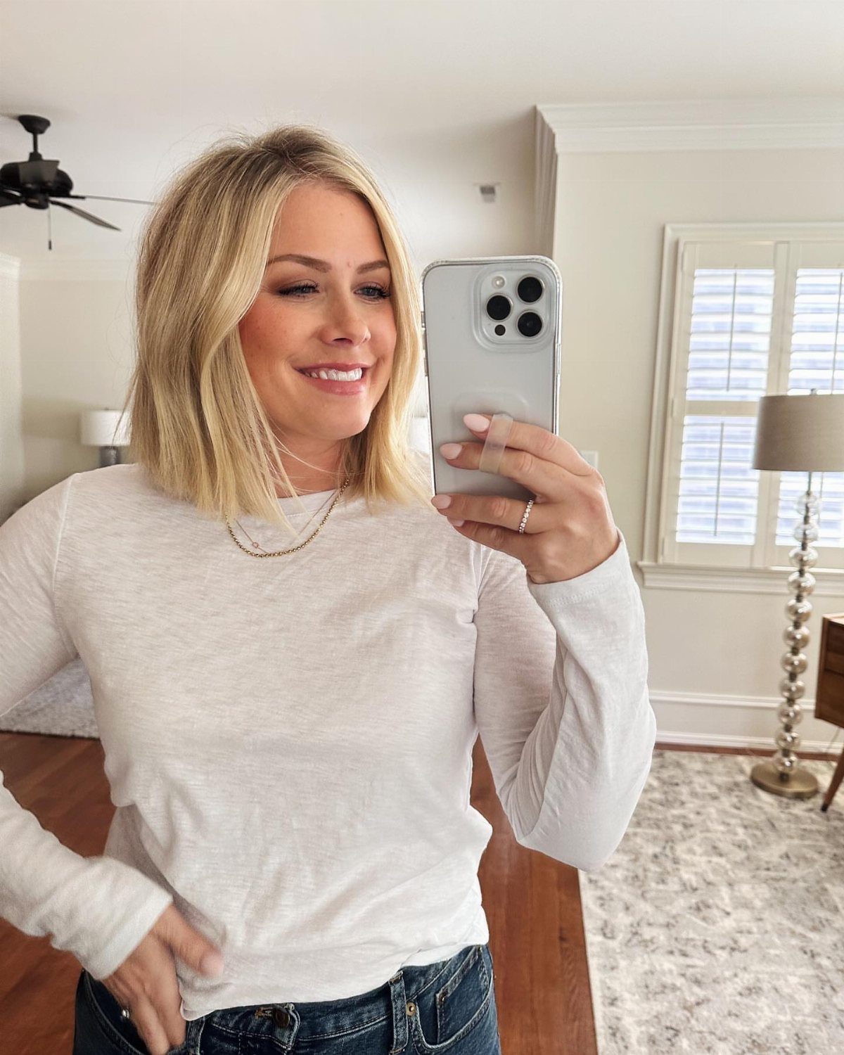 Woman with a blonde blunt lob haircut taking a mirror selfie in a room.