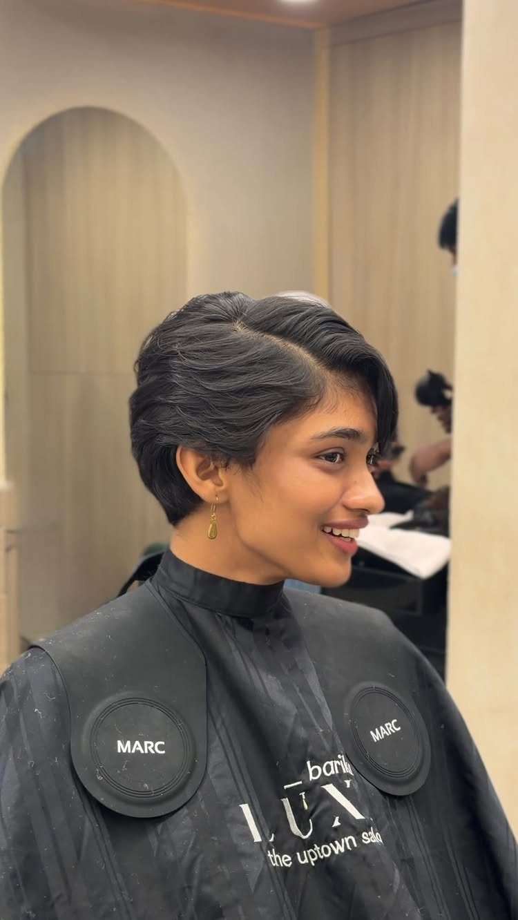Woman with a short, dark, side-parted haircut smiling in a hair salon.
