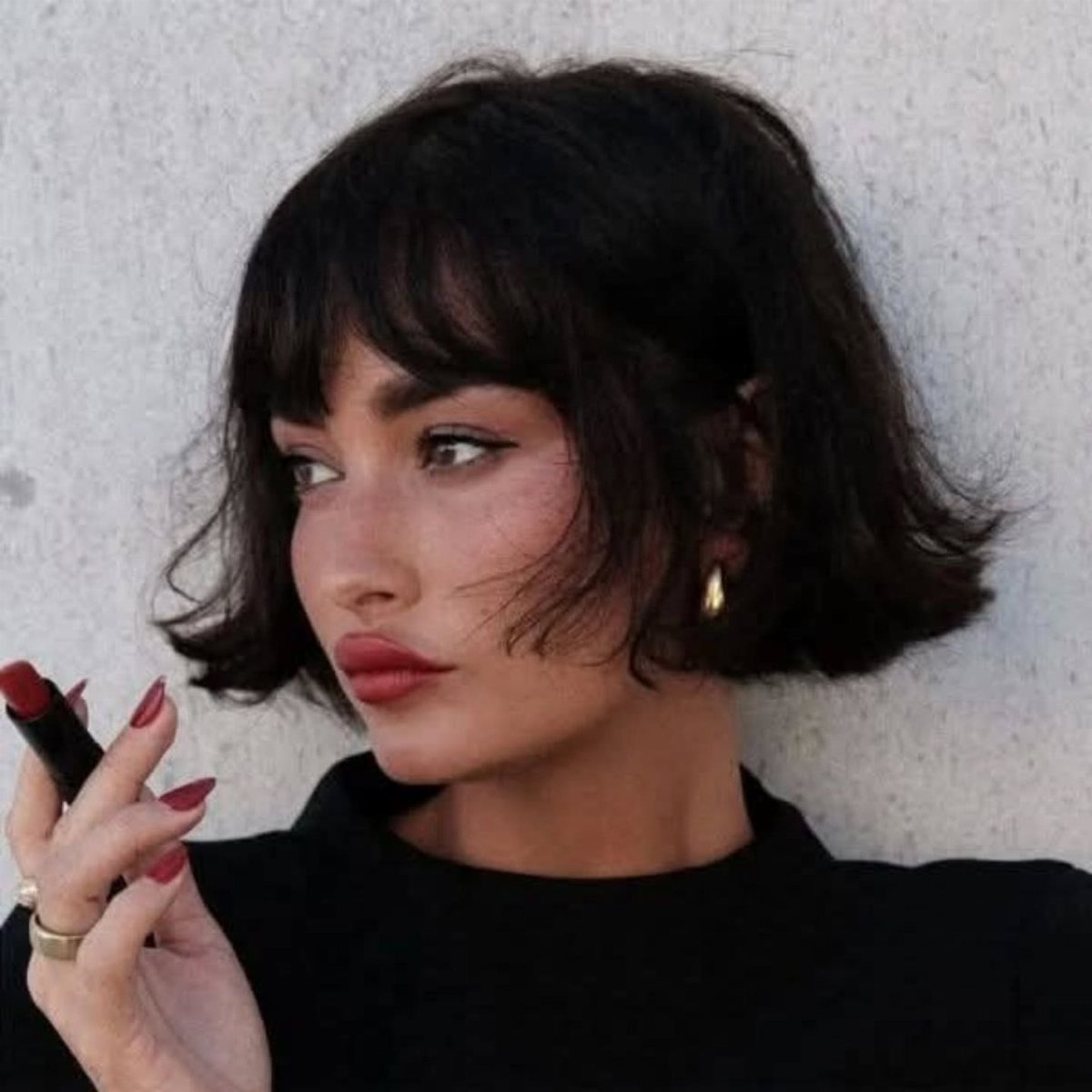Woman with a short dark brown French bob and bangs wearing red lipstick.