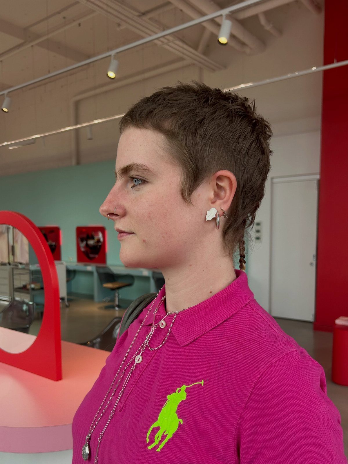 Person with a very short textured brown micro pixie haircut wearing a pink polo.