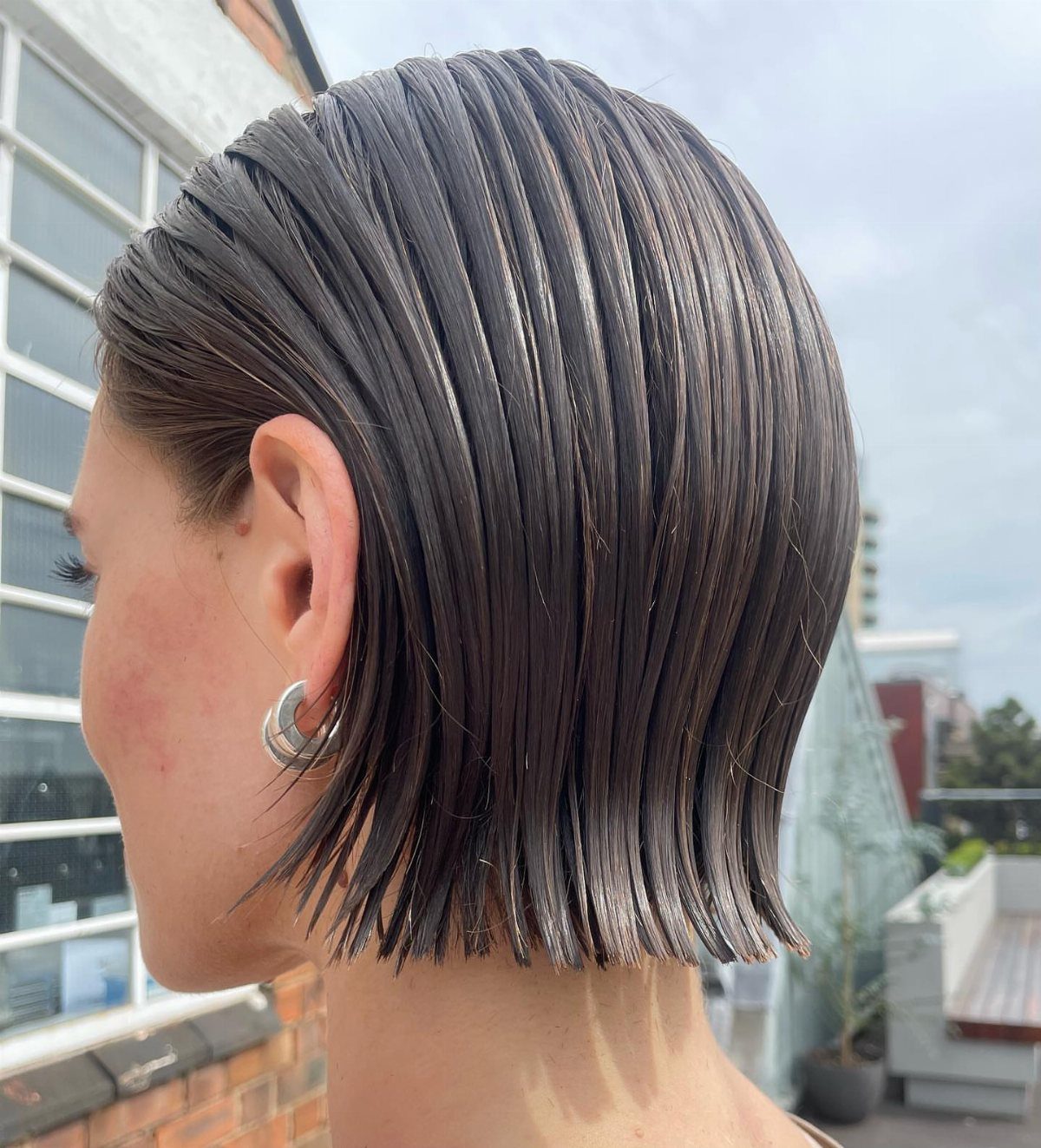 Slicked-back short dark hair with a wet look and blunt ends at the neck.