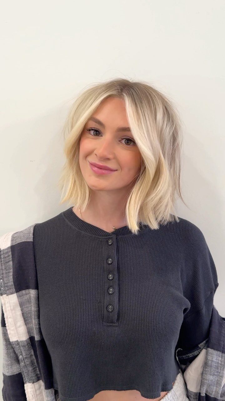 Woman with a blonde textured bob haircut and soft waves against a white wall.
