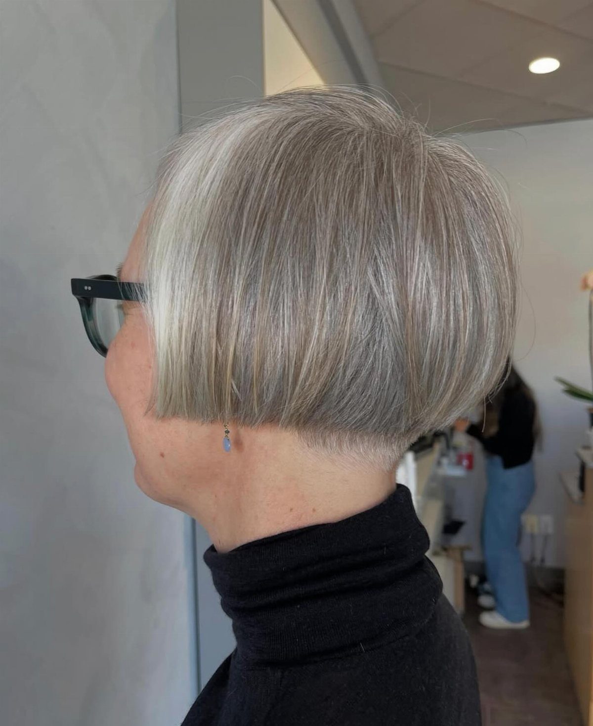 Older woman with a short, blunt silver bob haircut and black glasses.