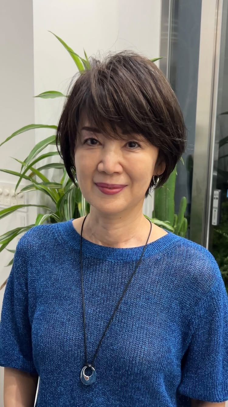Woman with a short brown layered bob hairstyle and blue knit top.