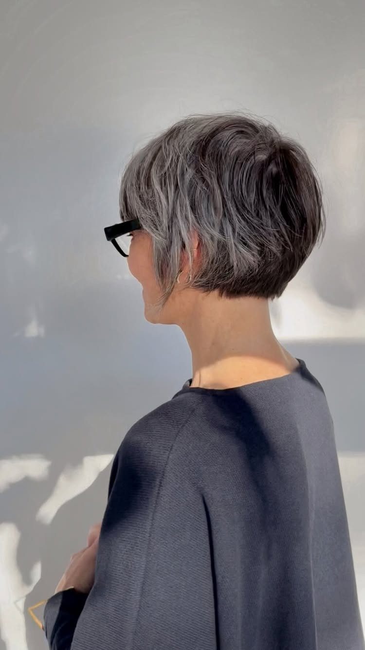 Older woman with a short layered grey hairstyle and black glasses in profile
