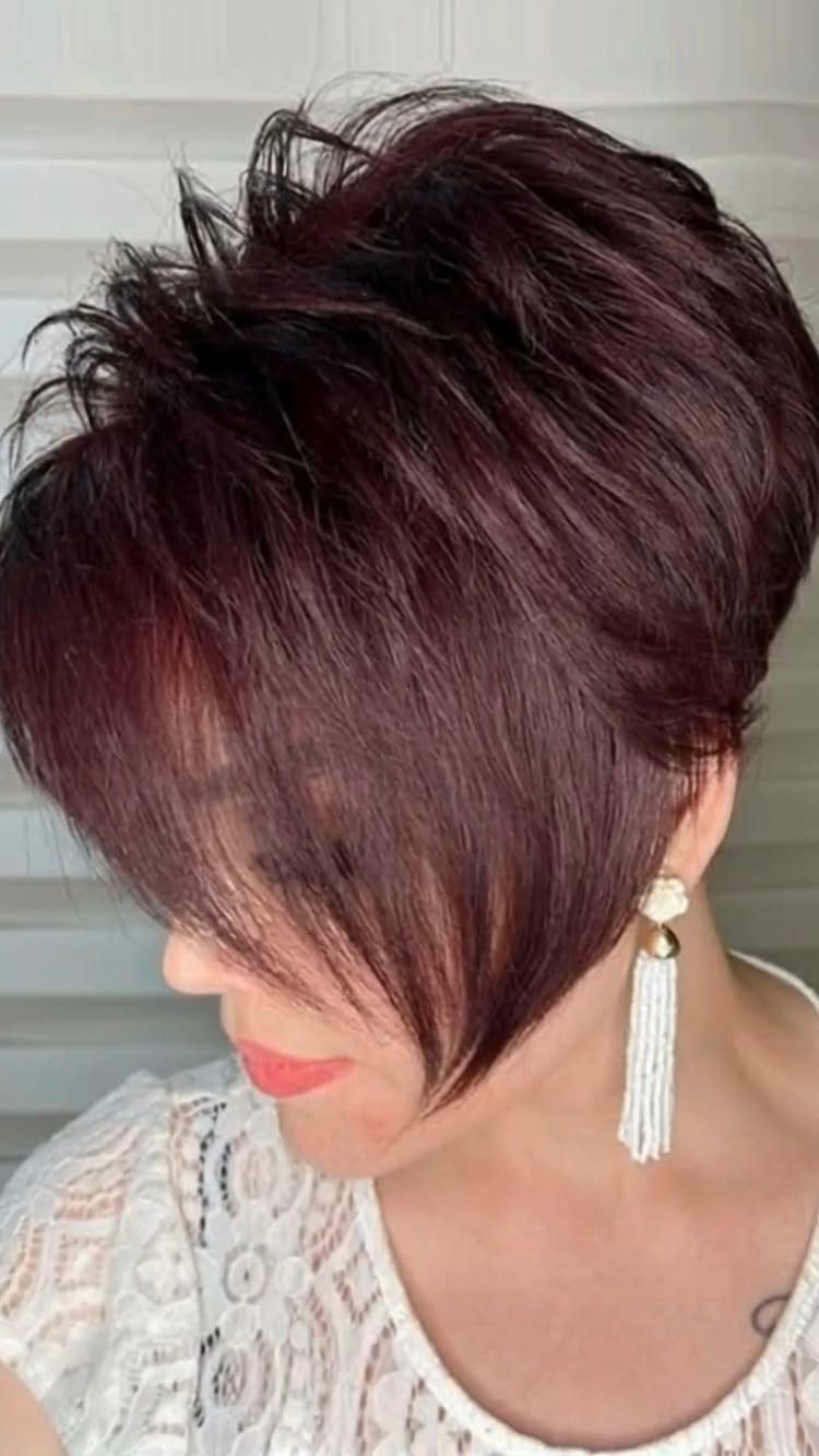 Woman with a burgundy textured pixie haircut and long white beaded earrings.