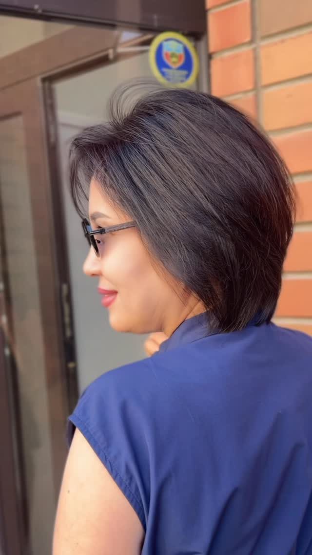 Woman with a short, voluminous dark brown bob haircut and black glasses.