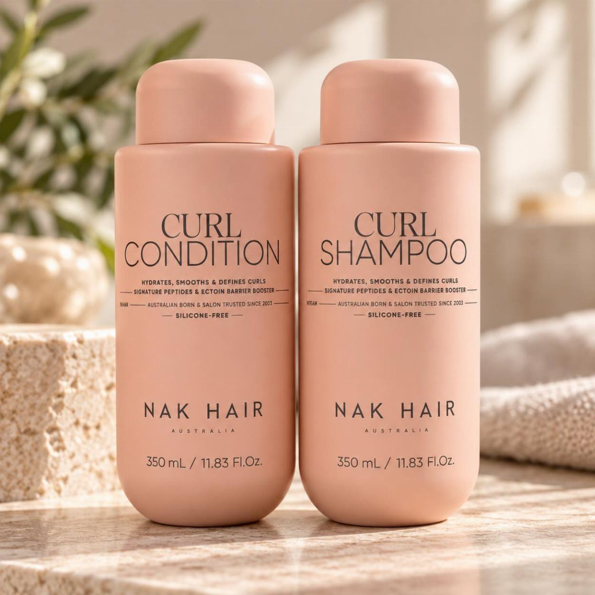 NAK Hair Curl Shampoo and Conditioner bottles in peach on a stone surface.