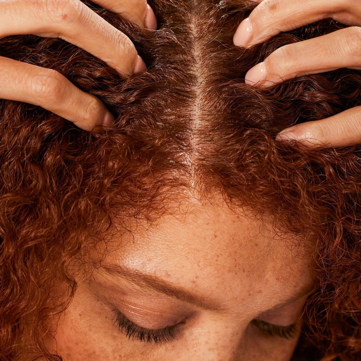Person with curly red hair receiving a scalp massage along the center part.