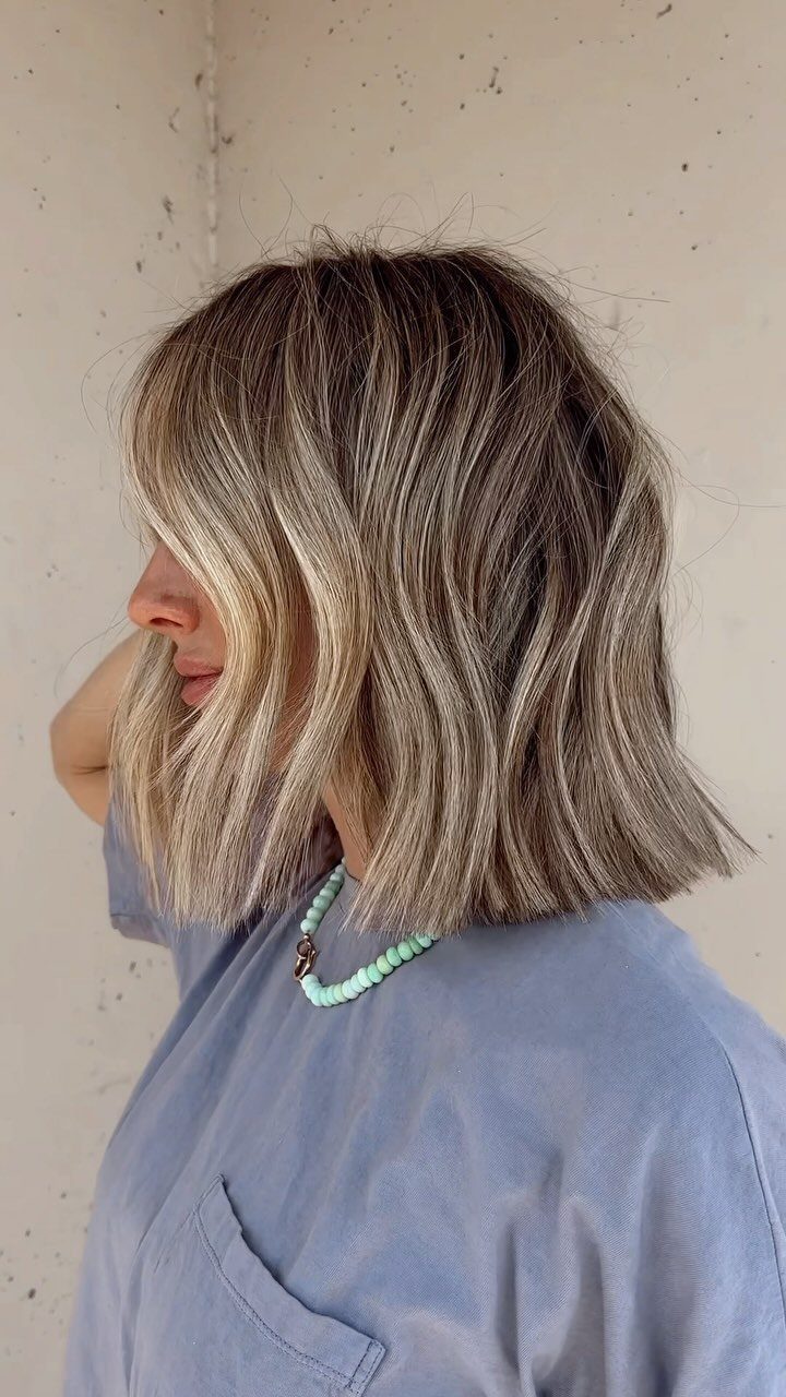 Woman with a blonde wavy bob haircut and a blue beaded necklace.