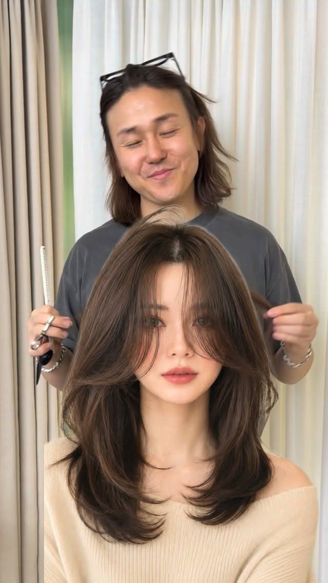 Woman with brown hair and face-framing layers being styled by a male hairdresser.