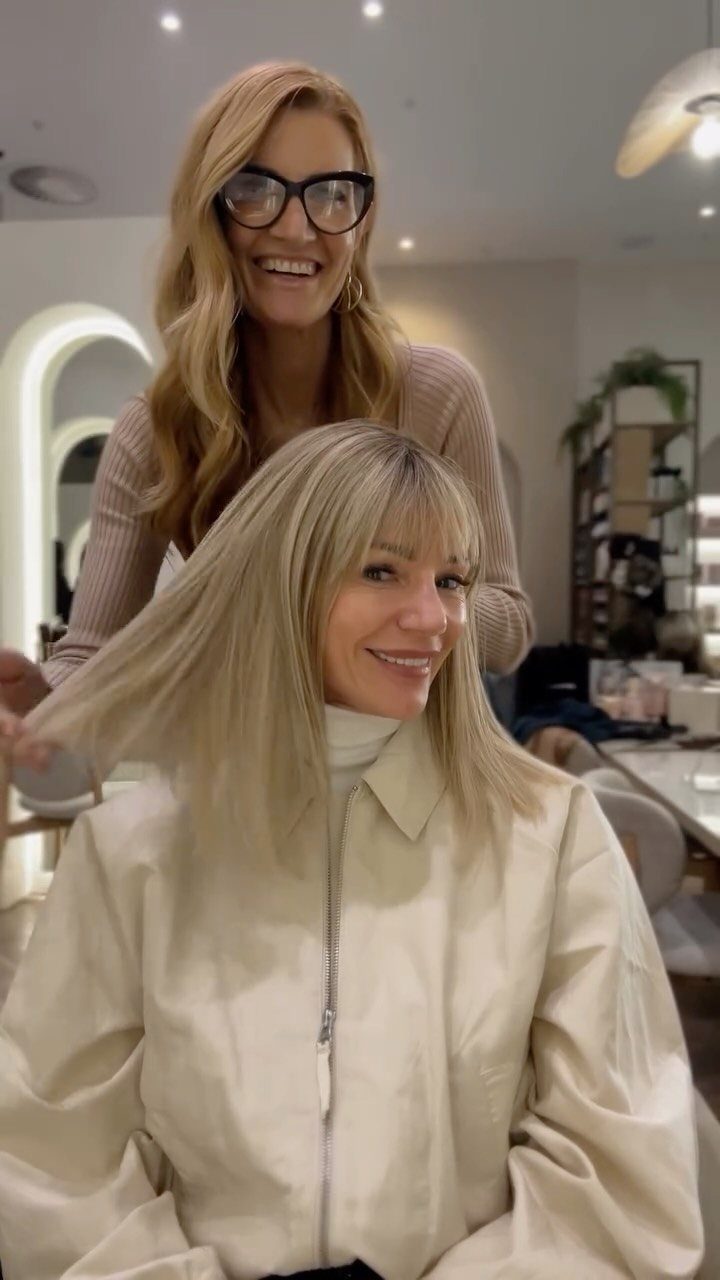 Blonde woman with a full fringe hairstyle posing with her hair stylist.