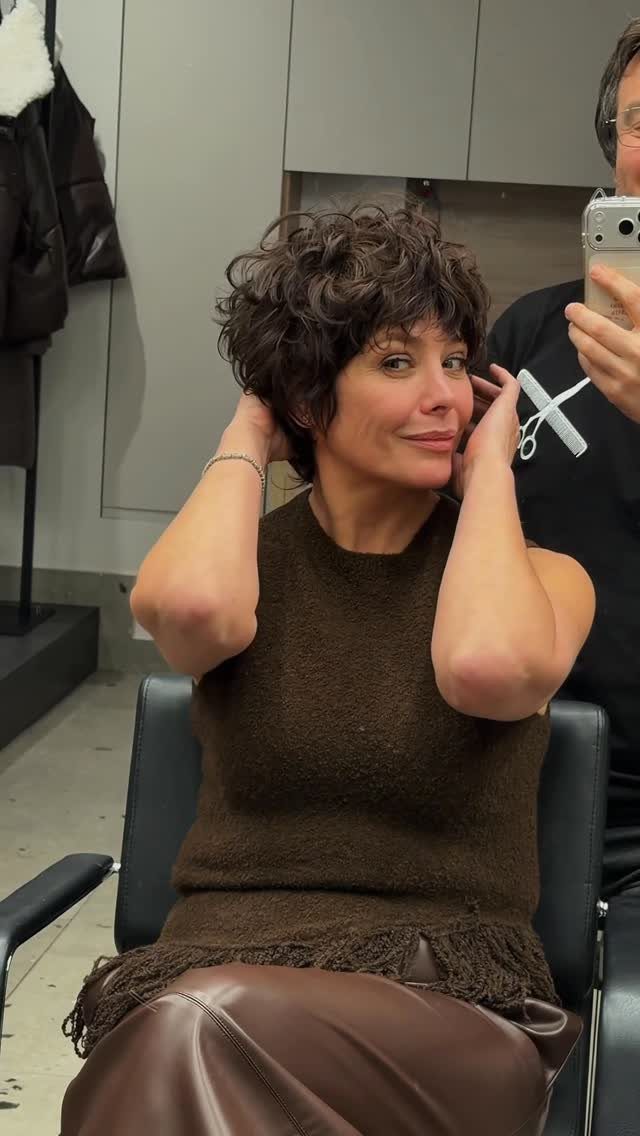Woman with a curly brown pixie-bob haircut posing in a hair salon chair.