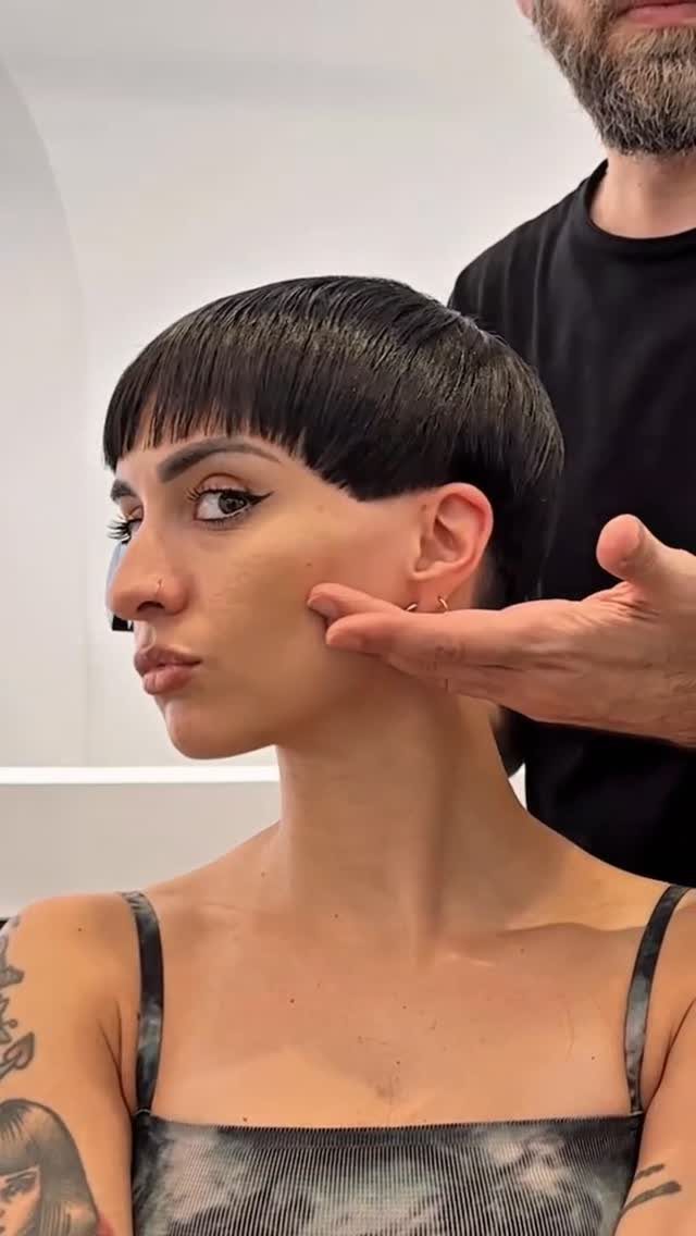 Woman with a dark pixie cut and blunt fringe in a salon setting.
