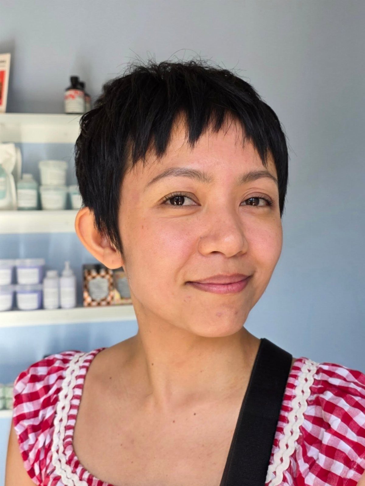 Woman with a short, dark textured pixie cut and choppy bangs smiling.