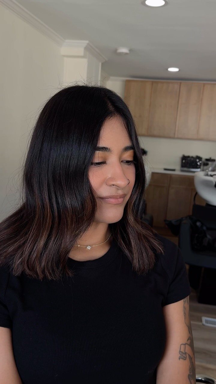 Woman with a dark brown wavy lob haircut and a center part.
