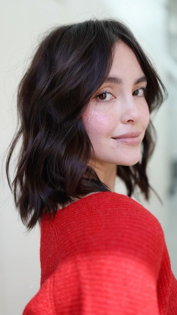 Woman with wavy dark brown long bob haircut wearing a red sweater.