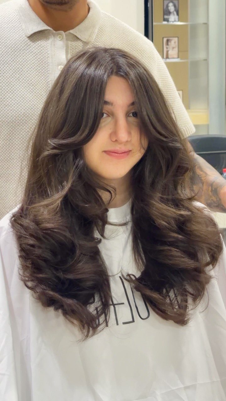 Woman with long brown wavy hair featuring voluminous layers and curtain bangs.