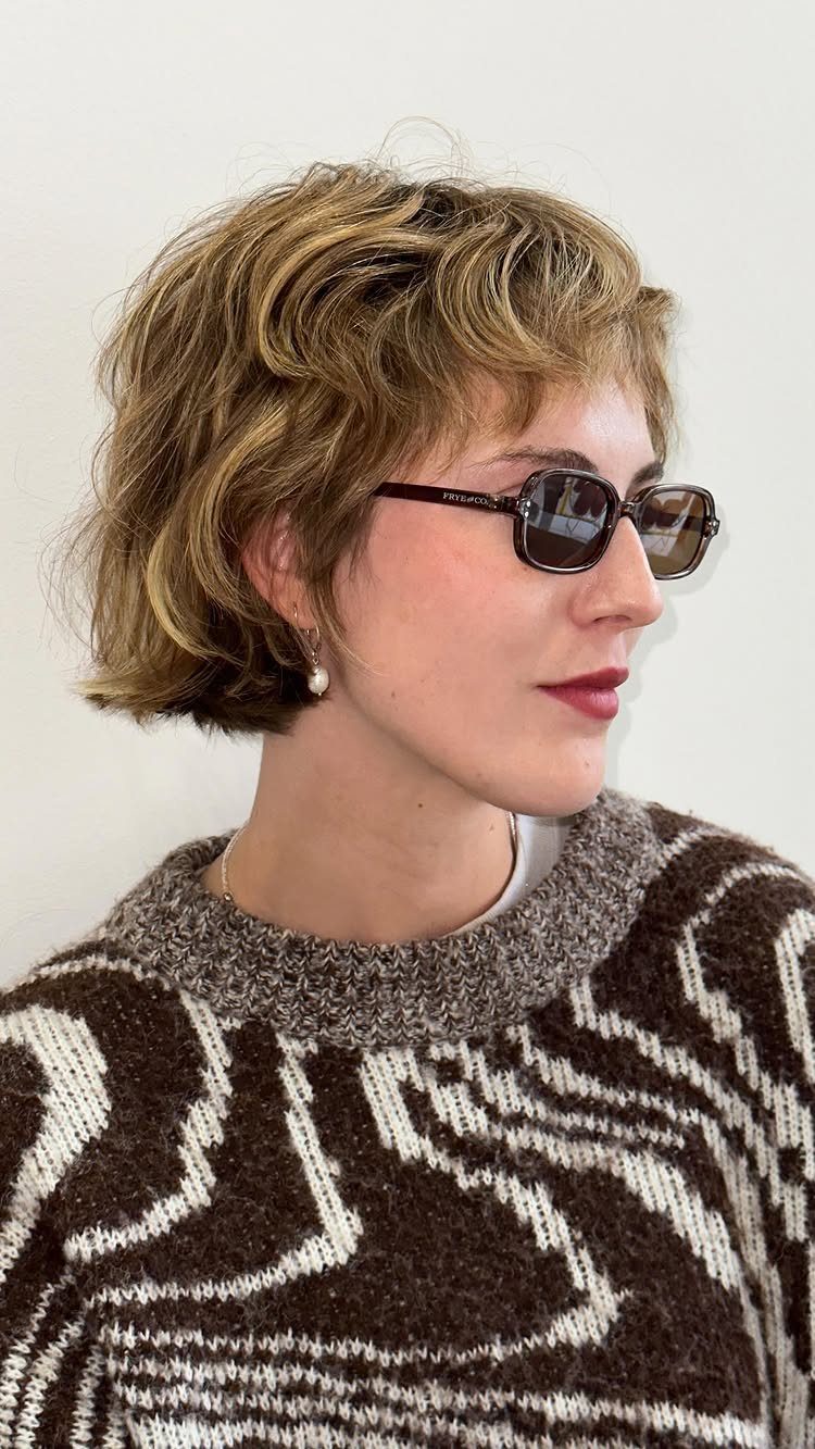 Woman with a blonde shaggy bob haircut and bangs wearing dark sunglasses.